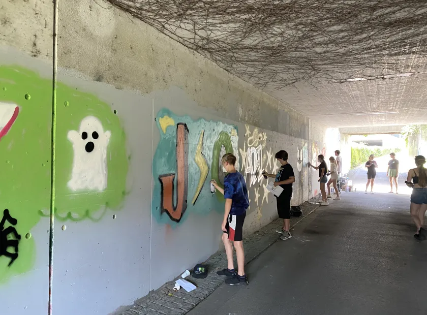 Jugendliche stehen an der Wand und sprayen farbige Graffitis. 